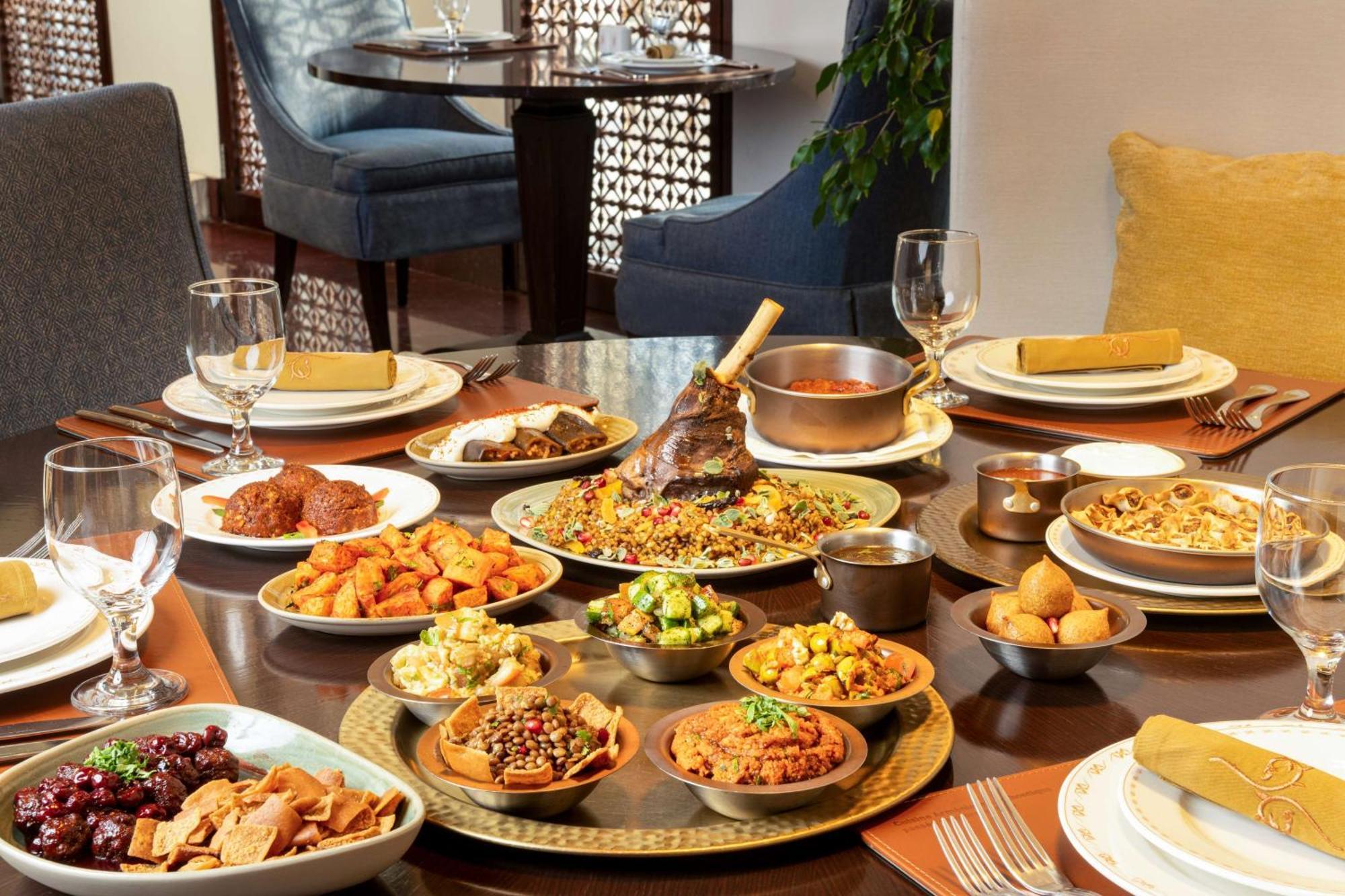 Hilton Riyadh Hotel & Residences Exterior foto The photo depicts a beautifully arranged dining table featuring a variety of dishes. There are several large plates filled with different foods, including a prominent dish at the center that appears to be rice and meat, likely a type of biryani or pi